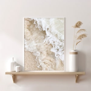 May include: A framed print of a close-up of a sandy beach with white foamy waves crashing on the shore.