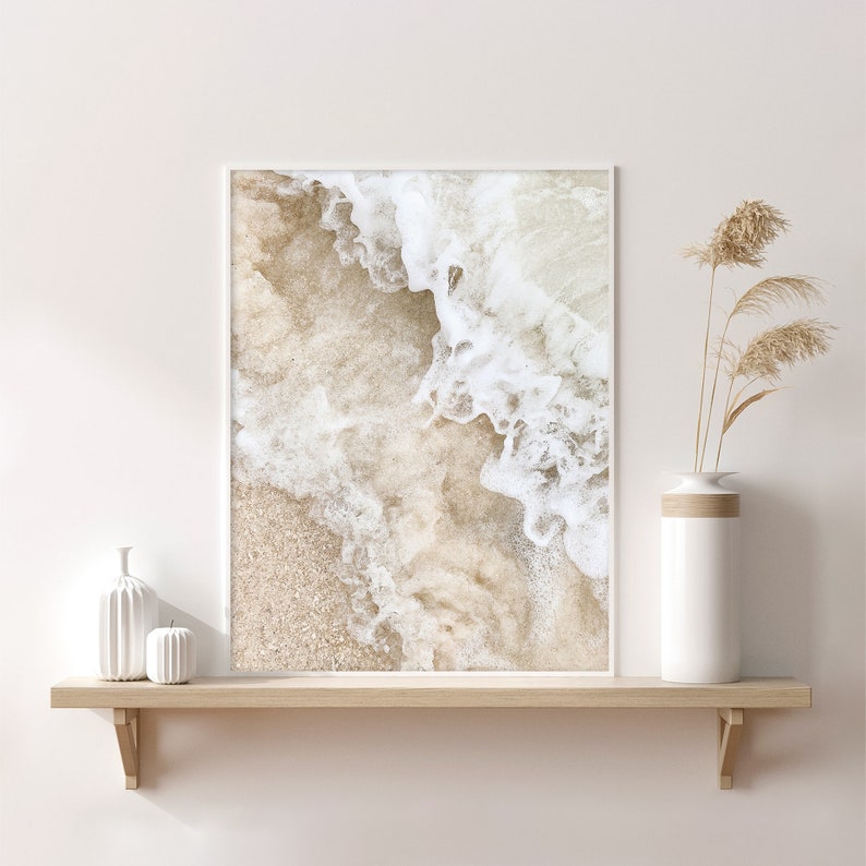 May include: A framed print of a close-up of a sandy beach with white foamy waves crashing on the shore.