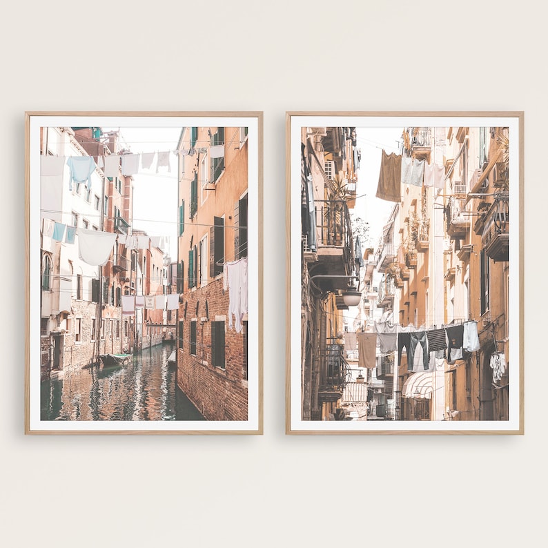 May include: Two framed prints of narrow, colorful streets in Italy with laundry hanging on lines across the buildings. The left print shows a canal with a gondola. The right print shows a street with a cobblestone path.