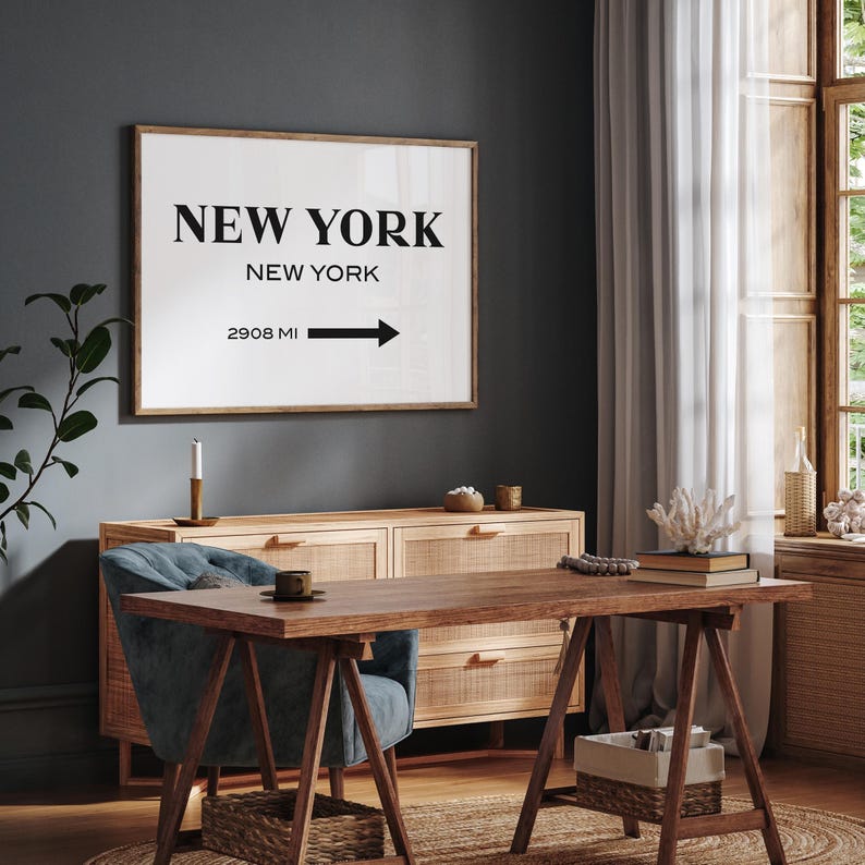 May include: A rectangular wall art print in a wooden frame featuring the text NEW YORK, NEW YORK and 2908 MI with a black arrow pointing to the right. The print has a white background with bold black lettering, displayed on a dark gray wall.