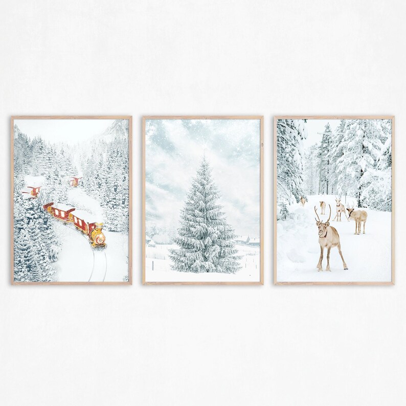 May include: A set of three framed wall art prints featuring winter scenes. The left print shows a red train traveling through a snowy forest. The center print depicts a large snow-covered pine tree. The right print shows reindeer in a snowy landscape.