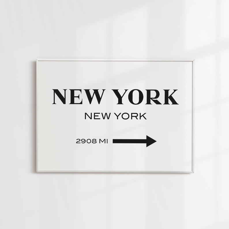 May include: A rectangular wall art print in a thin frame featuring the text NEW YORK in large black serif font, followed by NEW YORK in smaller sans-serif font, and the text 2908 MI with a black arrow pointing to the right on a white background.