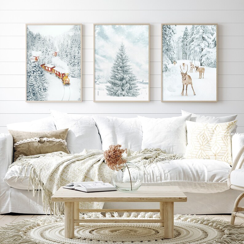 May include: Three framed wall art prints featuring winter scenes. The left print shows a red train in a snowy forest. The center print depicts a snow-covered pine tree. The right print displays a group of reindeer standing in a snowy landscape.