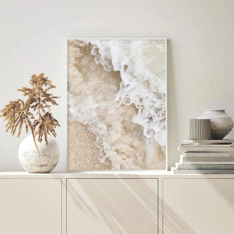 May include: A framed print of a close-up of white ocean waves crashing on a sandy beach. The image is in shades of beige and white.