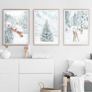 May include: Three framed wall art prints featuring winter scenes. The left print shows a red train in a snowy forest. The center print depicts a large snow-covered pine tree. The right print displays a group of reindeer in a snowy landscape.