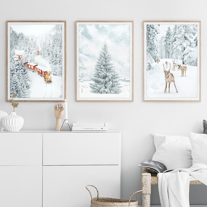 May include: Three framed wall art prints featuring winter scenes. The left print shows a red train in a snowy forest. The center print depicts a large snow-covered pine tree. The right print displays a group of reindeer in a snowy landscape.