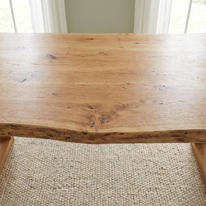 Pode incluir: Uma mesa de madeira castanha clara com uma borda viva. A mesa tem um gr&atilde;o de madeira natural e &eacute; suportada por pernas de madeira. A mesa tem aproximadamente 152 cm de comprimento e 76 cm de largura.