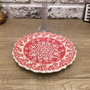Puede incluir: Un plato de cer&aacute;mica blanco con un dise&ntilde;o floral rojo y blanco. El plato tiene un borde festoneado y est&aacute; decorado con un patr&oacute;n repetitivo de flores y hojas.