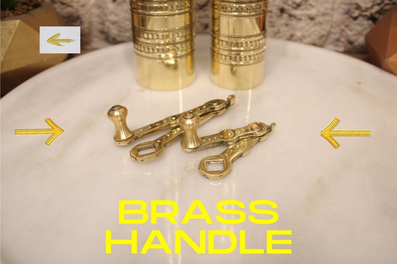 May include: Two gold-toned brass handles with a decorative design. The handles are on a white marble surface. The text "BRASS HANDLE" is written in yellow letters below the handles.