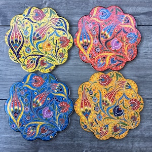 May include: Four round ceramic coasters featuring a floral pattern. The coasters are yellow, blue, red, and orange with intricate designs.