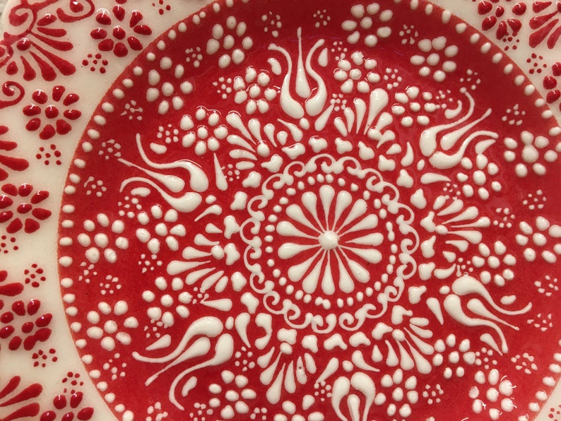 Puede incluir: Un plato de cer&aacute;mica rojo con un dise&ntilde;o floral blanco. El dise&ntilde;o presenta intrincados remolinos y puntos.