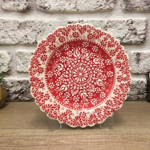 Puede incluir: Un plato de cer&aacute;mica blanco con un dise&ntilde;o floral rojo y blanco. El plato tiene un borde festoneado y est&aacute; decorado con intrincados patrones.
