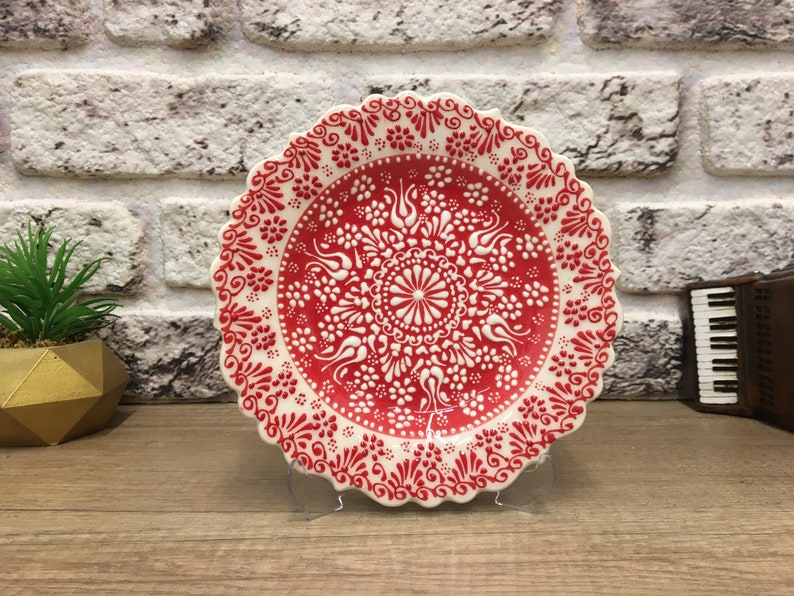 Puede incluir: Un plato de cer&aacute;mica blanco con un dise&ntilde;o floral rojo y blanco. El plato tiene un borde festoneado y est&aacute; decorado con intrincados patrones.