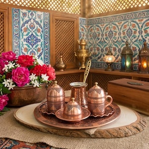 May include: A copper Turkish coffee set with a traditional design. The set includes a coffee pot, four cups, and a sugar bowl. The set is on a wooden tray with a decorative design.