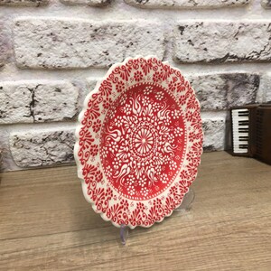 Puede incluir: Un plato de cer&aacute;mica blanco con un dise&ntilde;o floral rojo y blanco. El plato tiene un borde festoneado y est&aacute; sobre una superficie de madera.