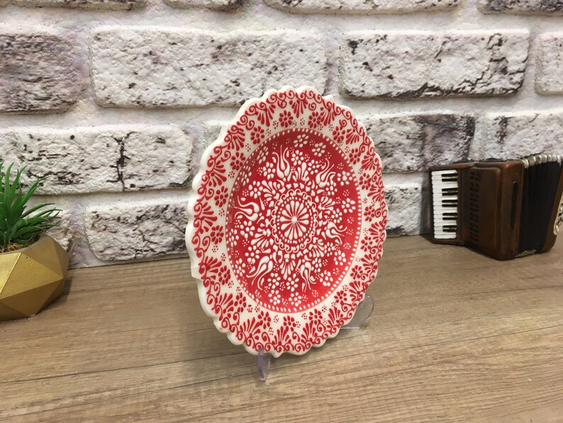 Puede incluir: Un plato de cer&aacute;mica blanco con un dise&ntilde;o floral rojo y blanco. El plato tiene un borde festoneado y est&aacute; sobre una superficie de madera.
