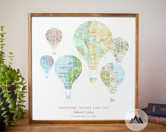 May include: A framed print with a white background featuring a design of hot air balloons made from vintage maps. The balloons are in shades of blue, green, and pink. The text "Adventuring Together Since 1972 Robert & Julie Celebrating 50 Years" is printed below the balloons.