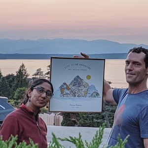 May include: A couple poses in front of a mountain range with a framed print that reads "Life is an adventure, best traveled together." The print features a stylized mountain range with a sun and the text "Farris & Lamar Est. 2018."