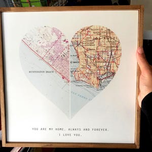 K&ouml;nnte beinhalten: Ein gerahmter Druck einer herzf&ouml;rmigen Karte von Los Angeles, Kalifornien. Die Karte ist in zwei H&auml;lften geteilt, wobei die linke Seite Huntington Beach und die rechte Seite die Stadt Los Angeles zeigt. Der Text "You are my home, always and forever. I love you." ist unter der Karte gedruckt.