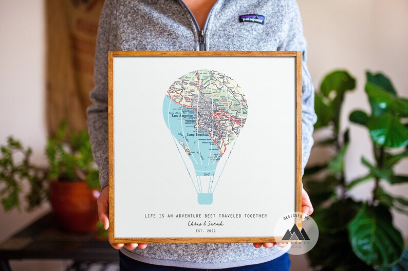 May include: A framed print with a vintage map of Los Angeles, California, shaped into a hot air balloon. The print has the text "Life is an adventure best traveled together" and "Chris & Sarah Est. 2022".
