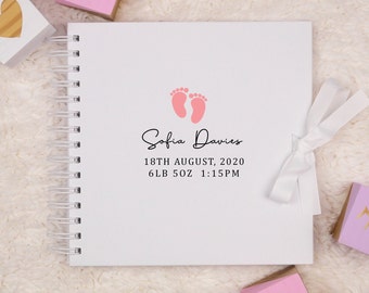 May include: A white baby memory book with a pink footprint design and the text "Sofia Davies 18th August, 2020 6LB 5OZ 1:15PM".