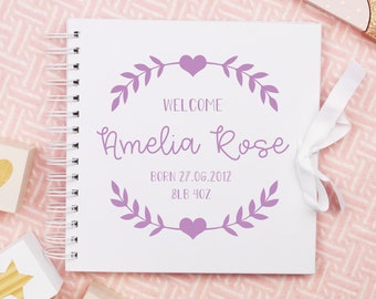 May include: White baby memory book with a purple ribbon and a purple floral design. The book says "Welcome Amelia Rose Born 27.06.2012 8LB 4OZ".
