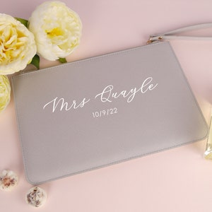 May include: A grey clutch bag with a white zipper and a white strap. The bag has the text "Mrs. Quayle" and the date "10/9/22" printed on it.