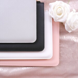 May include: Four different colored zippered pouches stacked on top of each other. The pouches are white, black, white, and pink. The pouches are made of a smooth, textured material.