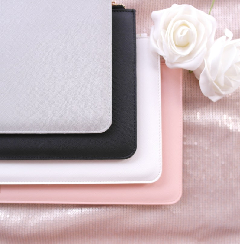 May include: Four different colored zippered pouches stacked on top of each other. The pouches are white, black, white, and pink. The pouches are made of a smooth, textured material.
