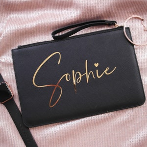 May include: Black clutch bag with a gold zipper and a gold inscription that reads "Sophie" with a small heart.