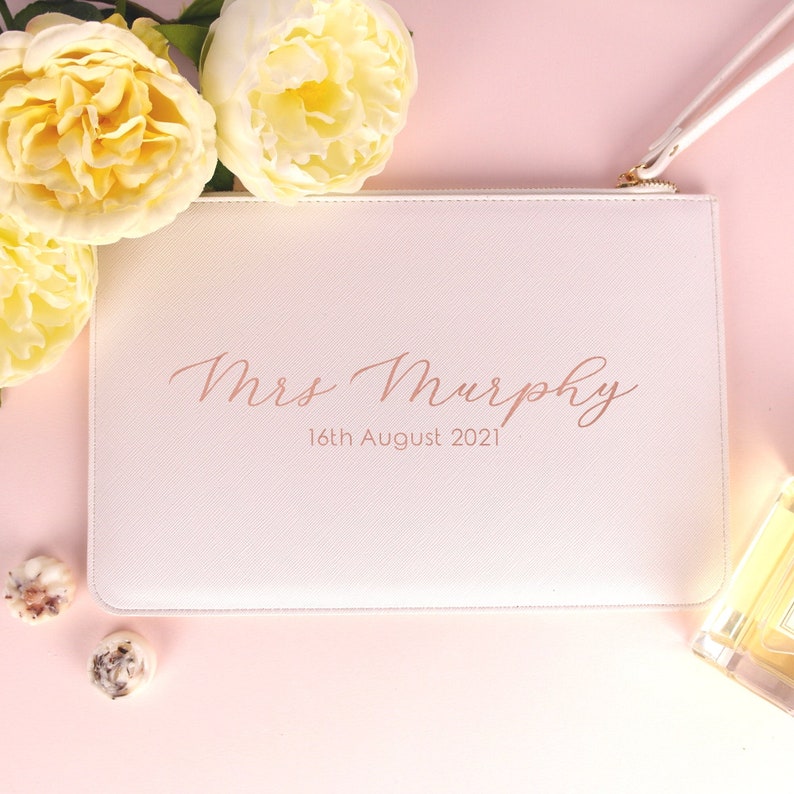 May include: White zippered pouch with a pink inscription that reads "Mrs. Murphy 16th August 2021".