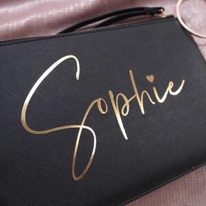 May include: Black clutch bag with a gold foil inscription that reads "Sophie" with a small heart.