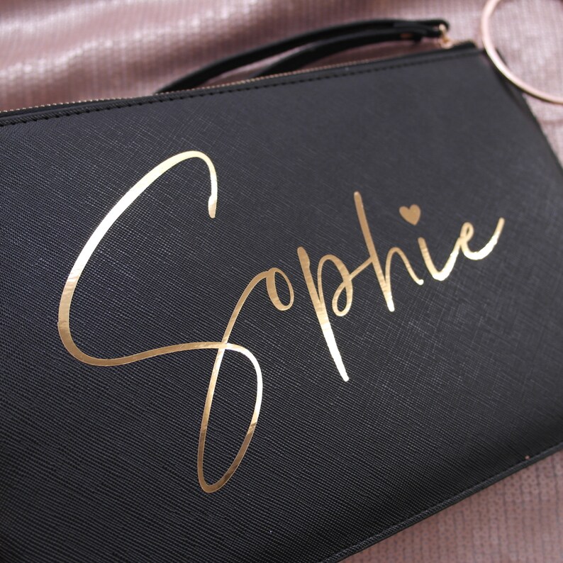 May include: Black clutch bag with a gold foil inscription that reads "Sophie" with a small heart.