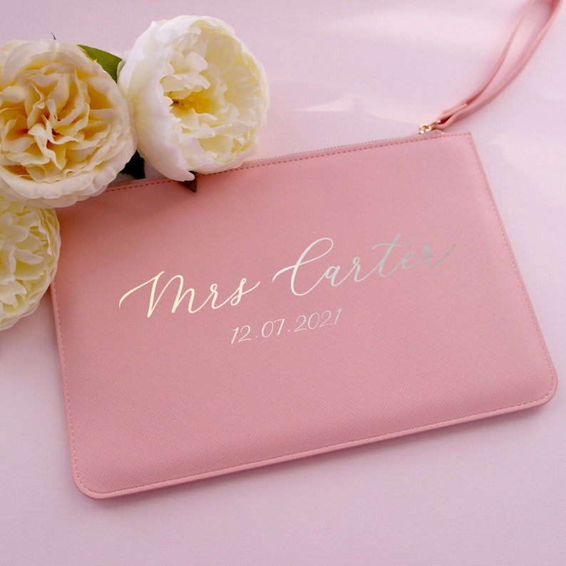 May include: A pink clutch bag with a silver inscription that reads "Mrs. Carter" and "12.07.2021".