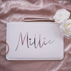 May include: White clutch bag with a silver zipper and a silver inscription that reads "Millie" with two small hearts.
