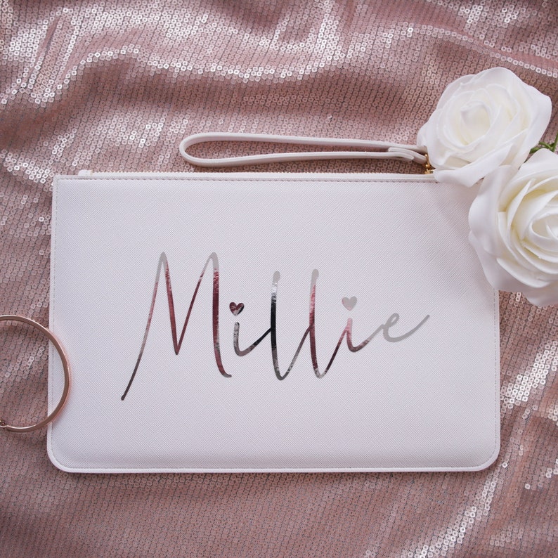May include: White clutch bag with a silver zipper and a silver inscription that reads "Millie" with two small hearts.