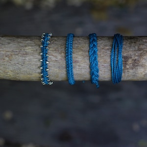 May include: Five blue bracelets made of different materials, including braided cord and beaded cord, are displayed on a wooden surface.