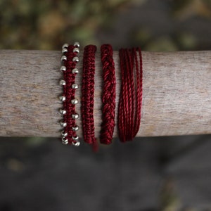 May include: Five red bracelets with different textures and patterns. One bracelet has silver beads.