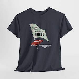 Peut inclure: T-shirt bleu marine foncé avec un motif rétro. Le graphisme comprend une voiture rouge, un drapeau avec le texte "America's Finest STOCK CAR RACES" et le texte "OCCONEECHEE SPEEDWAY HILLSBORO, NC 1953."