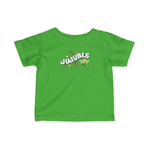 May include: A lime green toddler t-shirt with a crew neck. The shirt features the word "JUJUBES" in white, outlined in black, with colorful confetti and a cartoon bee graphic.