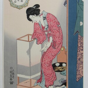 May include: Japanese woodblock print depicting a woman in a red patterned kimono, tending to a white lantern. The artwork features traditional Japanese calligraphy and a serene interior scene with a blue screen and tea set.