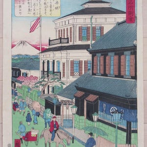 May include: A woodblock print depicting a street scene in Japan. The print features a white building with a red, white, and blue flag flying from the top. There are people walking on the street, some carrying umbrellas. The print is titled "Tokyo Famous Places Picture Book" in Japanese.