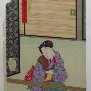 Op de afbeelding: Een Japanse houtsnede met een persoon in een paarse bloemenkimono met een rode riem met patroon, zittend achter een houten reling. De persoon houdt een klein groen voorwerp vast en raakt het gezicht aan. Tekst in rode en gele panelen.