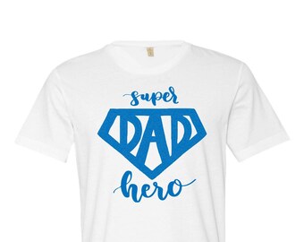 May include: White t-shirt with a blue superhero logo that says "super dad hero" in a stylized font.