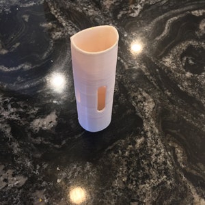 May include: A white plastic cylinder with two rectangular openings. The cylinder is sitting on a black and white countertop.