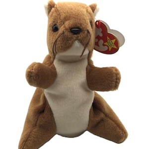 May include: A brown plush otter toy with a cream-colored belly and a red tag. The stuffed animal has a soft, furry texture and is designed to sit upright. The tag reads "Beanie Baby".