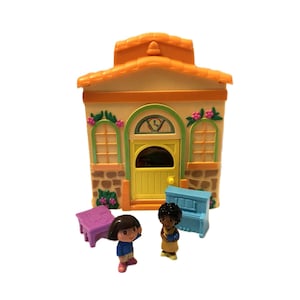 May include: A colorful toy playset featuring a house with an orange roof, yellow door, and green accents. Two figurines and miniature furniture, including a purple table and blue piano, are also included. The set is designed for children.