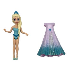 Pu&ograve; includere: Una bambola di un personaggio con i capelli biondi in una treccia laterale, che indossa un costume da bagno azzurro e una corona blu. Accanto alla bambola c'&egrave; un lungo mantello fluente nei toni del viola e del verde acqua.
