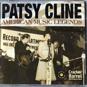 May include: A CD case featuring Patsy Cline, with the text "AMERICAN MUSIC LEGENDS." The image shows a vintage photo of Cline singing on stage with a band. The Cracker Barrel logo is visible.