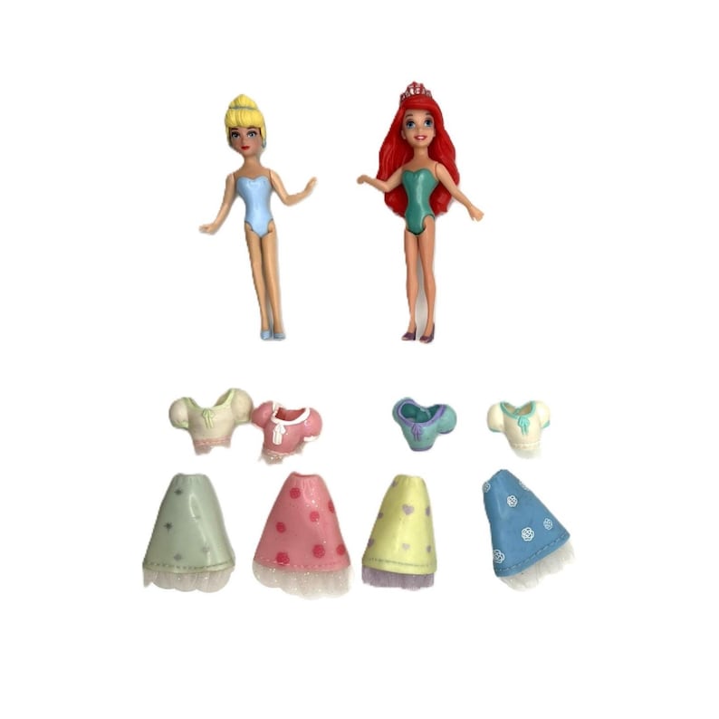 May include: Two small dolls, one with blonde hair and the other with red hair, wearing swimsuits. Below are several doll outfits, including tops and skirts in various pastel colors. The skirts have lace trim and heart or polka dot patterns.